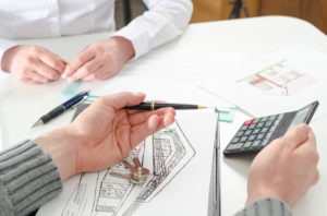 Realtor showing the home prices on a calculator to his client in real estate agency